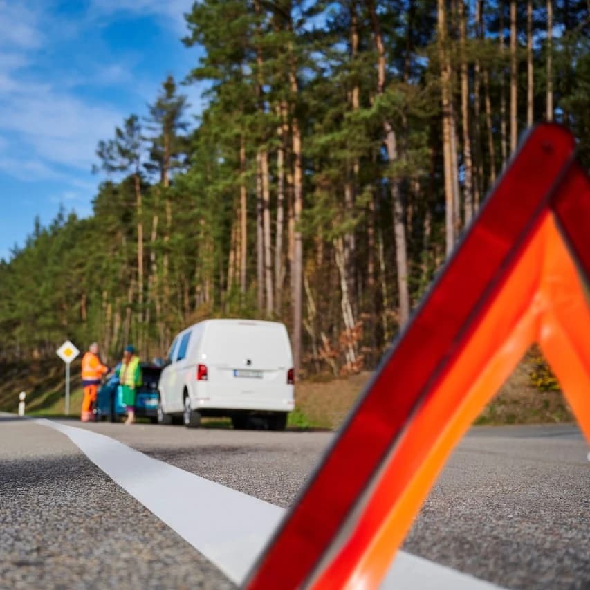 Trójkąt ostrzegawczy na drodze, w tle kolizja drogowa
