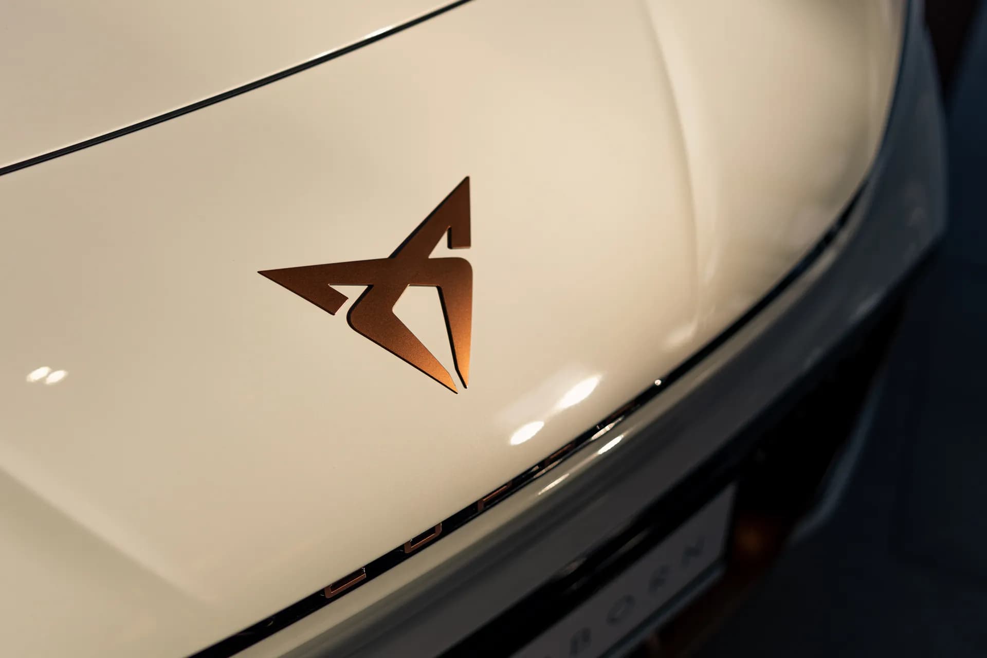 Zbliżenie miedzianego emblematu Cupra na masce białego modelu Born