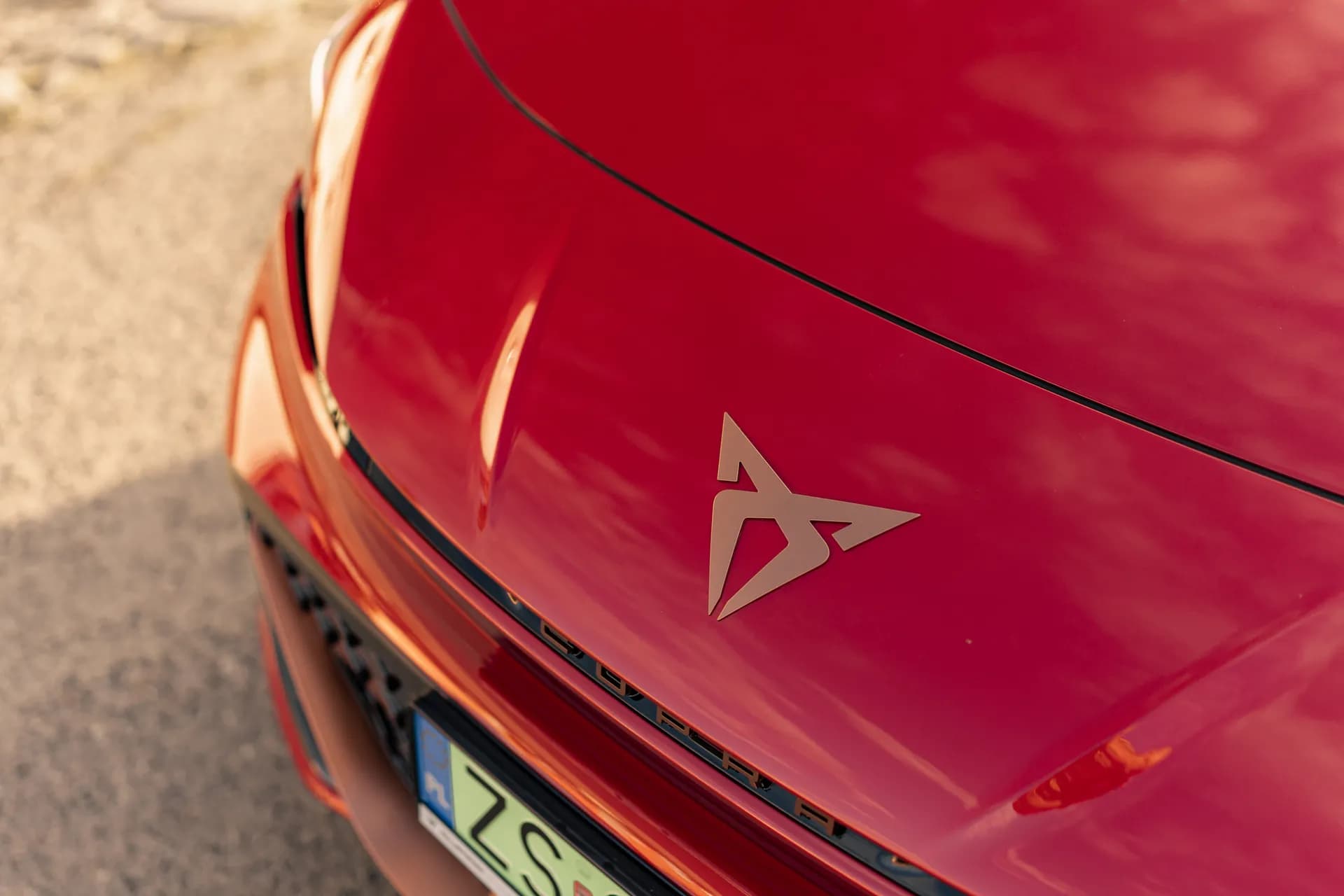 Miedziane logo Cupra na czerwonej masce samochodu – zbliżenie