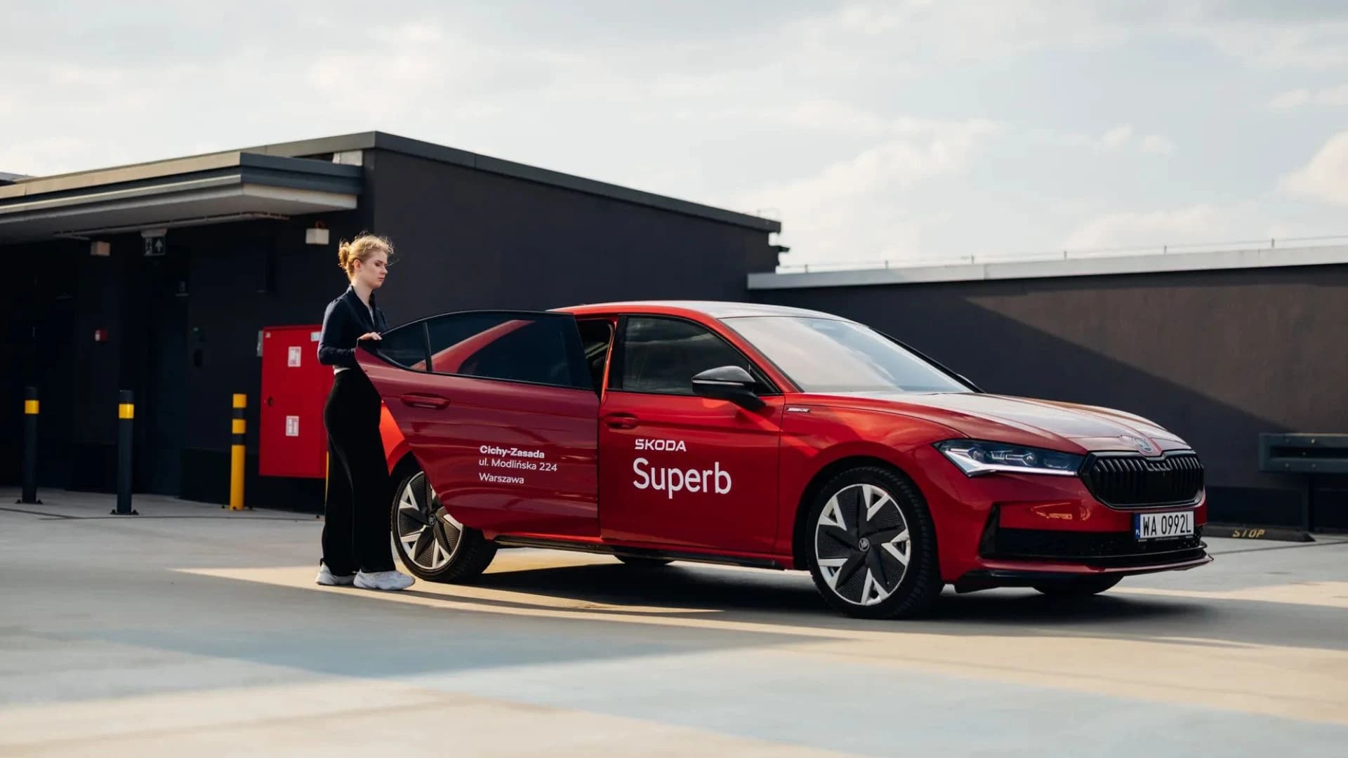 Jazda próbna Skoda Superb – konsultant otwiera drzwi czerwonego auta
