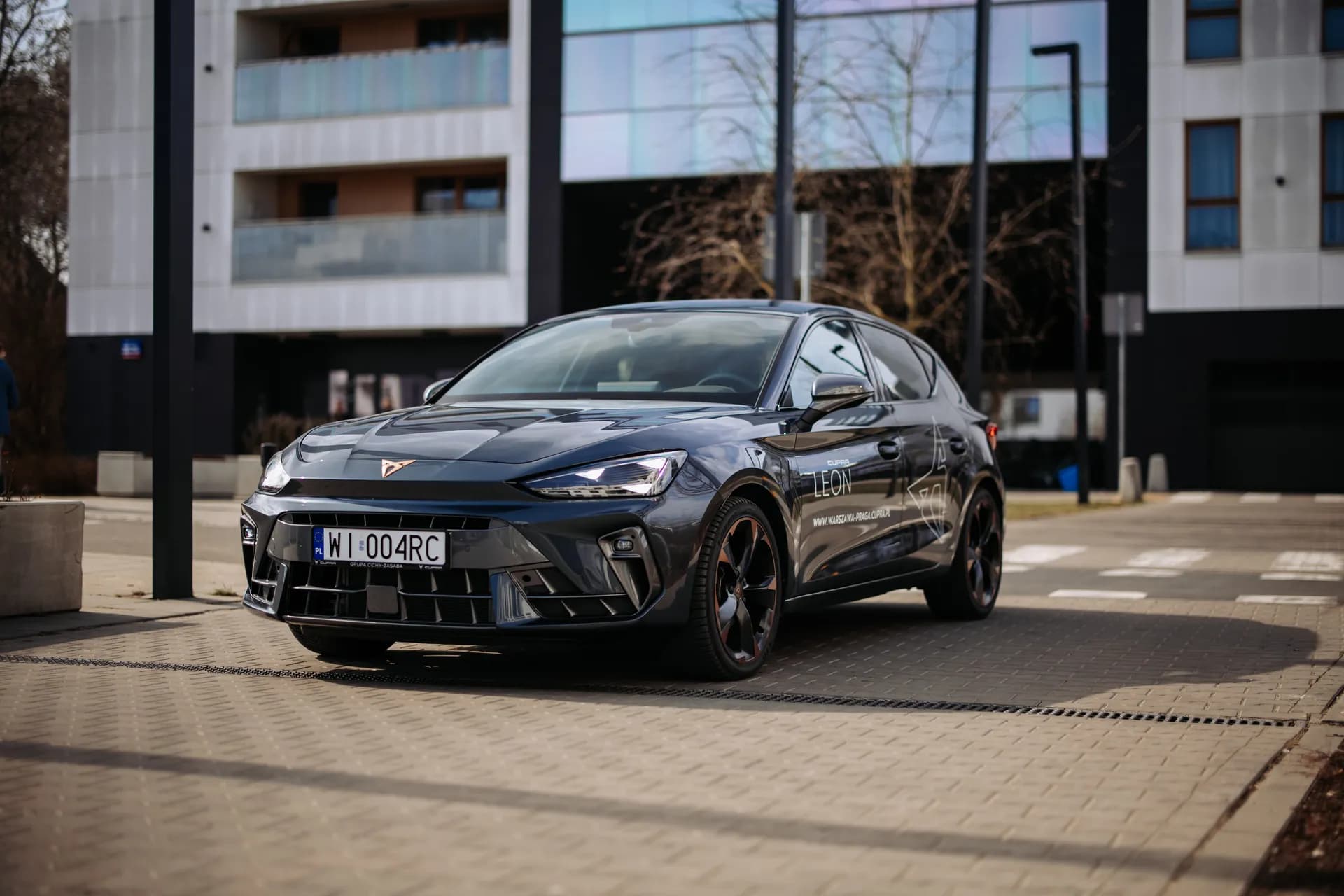 Szara Cupra Leon przed nowoczesnym budynkiem