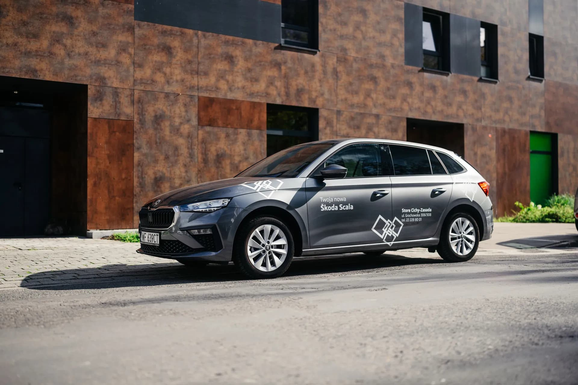 Szara Skoda Scala zaparkowana przed nowoczesnym budynkiem