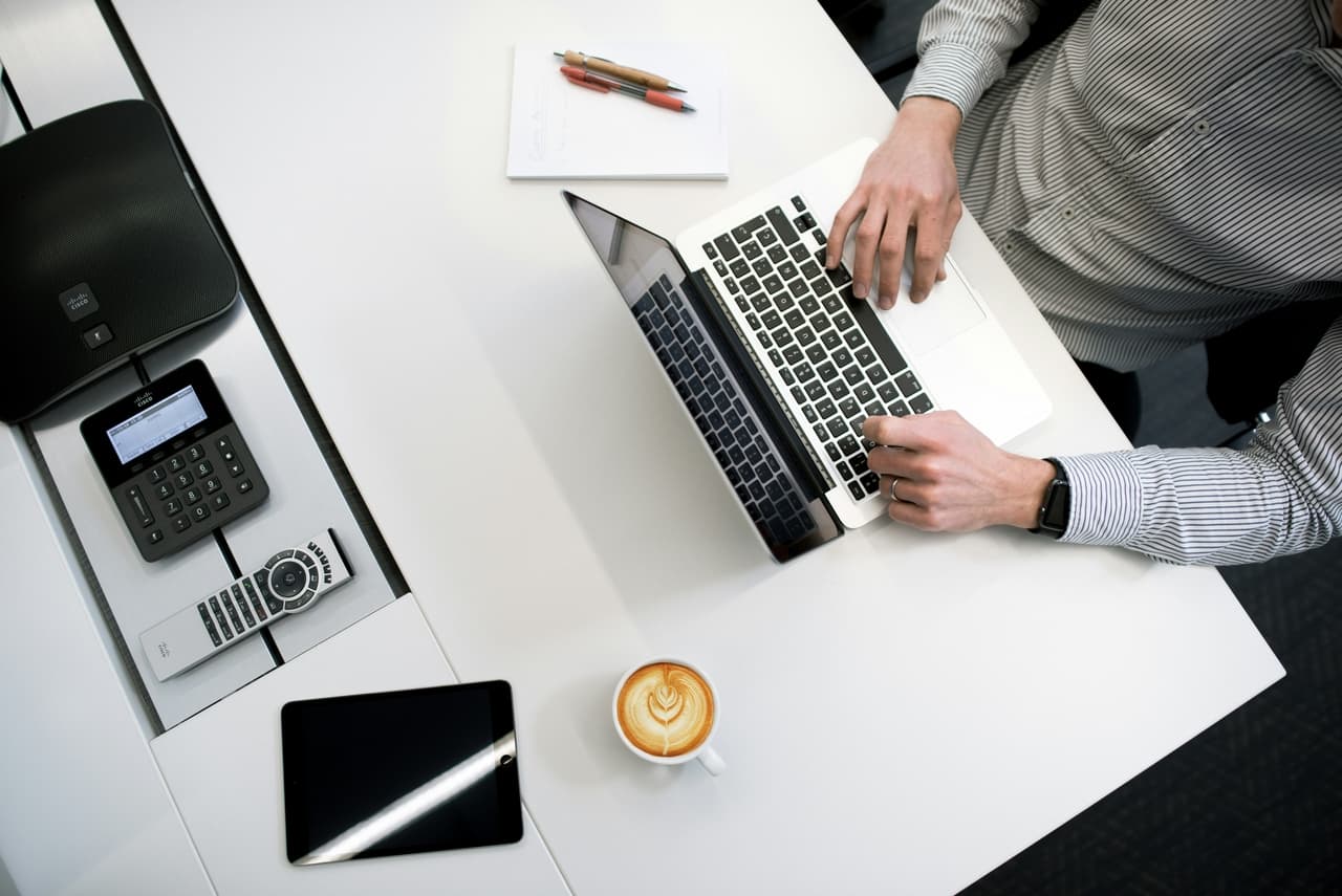 Mężczyzna siedzący przy biurku, pracujący na laptopie z kawą i notesem