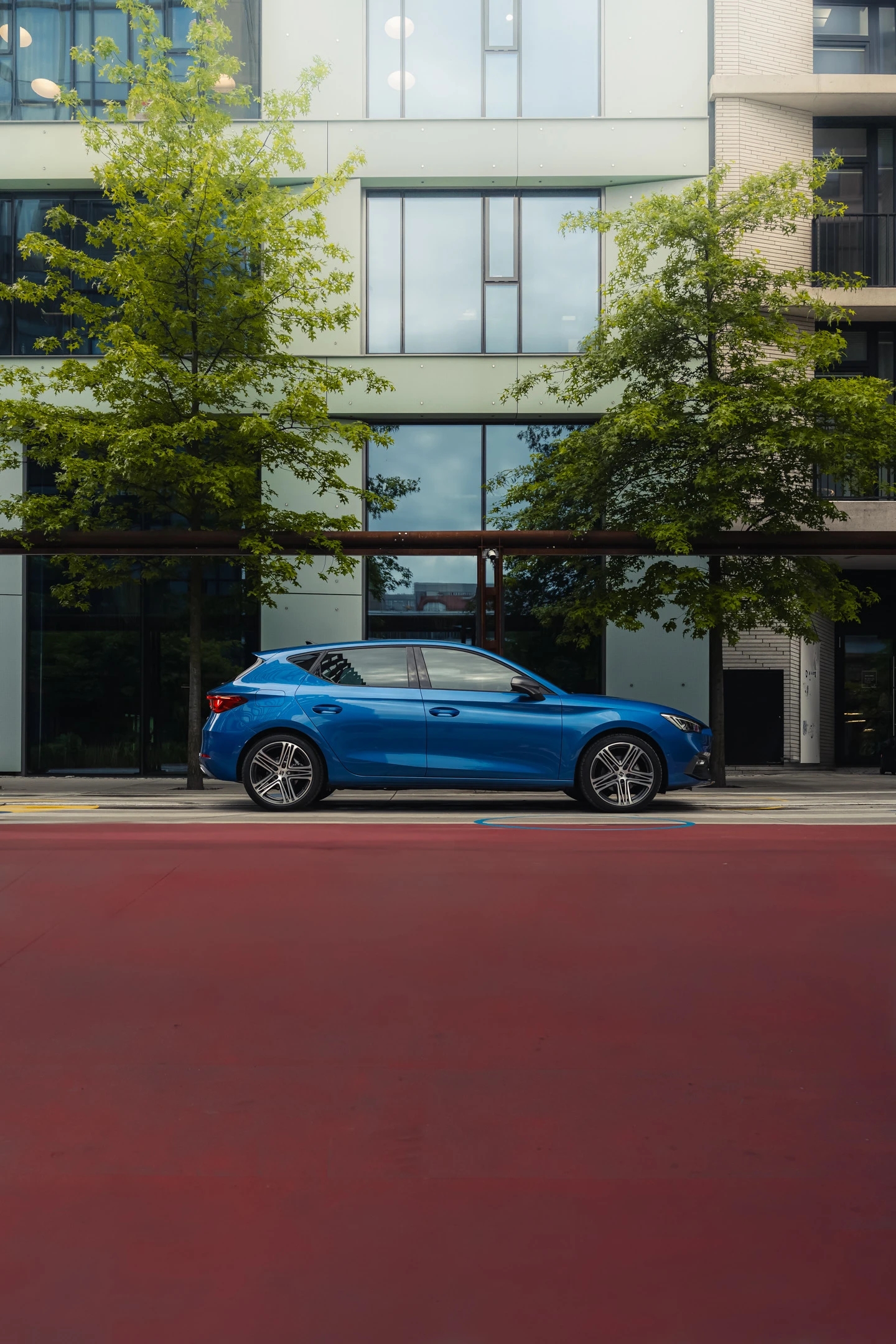 Niebieski SEAT Leon zaparkowany na tle przeszklonego biurowca