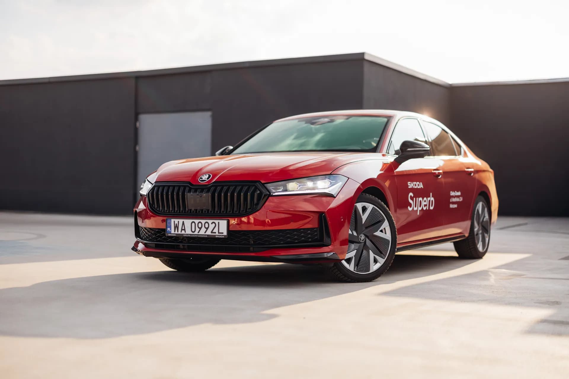 Czerwona Skoda Superb – profil boczny na parkingu dachowym